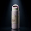 A  insulated water bottle by featuring a light lavender body with purple abstract line patterns, a beige paper label, and a pastel pink lid with a white flip-top straw cap, set against a dark background with a spotlight effect.