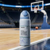 A Owala insulated water bottle with a light blue flip-top lid stands on a basketball court, with an empty arena and hoop blurred in the background.