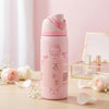 A pink Hello Kitty insulated water bottle with a matching pink lid, set on a wooden surface with soft pink roses and petals in a styled setting.