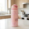 A pink Owala water bottle with Hello Kitty illustrations, standing on a white kitchen countertop with a blurred kitchen background.