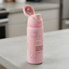 A pink Owala water bottle with a Hello Kitty design, standing on a light gray countertop with a blurred kitchen background.