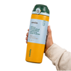 A hand holding an Owala insulated water bottle with a yellow body, dark green cap, and light blue label, shown against a plain white background.