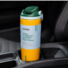 An Owala insulated tumbler with a yellow body, green lid, and light blue label, resting in a car cup holder.