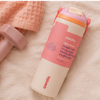 A pink and white Owala water bottle with a flip-top lid, styled on a soft beige fabric surface next to a pink towel and a pink dumbbell.