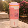 A 32 oz Owala leak-proof travel tumbler with a pink and white design, featuring a built-in straw lid, set on a stone surface with a blurred garden background.