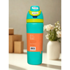 A Owala insulated water bottle with a bright blue body, orange and purple accents, and a yellow flip-top lid, standing on a wooden table with blurred flowers in the background.