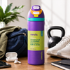 A purple Owala water bottle with a bright yellow-green label stands on a wooden table in a styled setting with a blue backpack, white earbuds, running shoes, a kettlebell, and a notebook nearby.