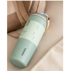 A Owala insulated tumbler in sage green and cream, shown resting on a beige fabric surface next to a matching beige bag.