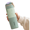 A hand holding a mint green Owala travel tumbler with a light purple lid and a beige sleeve on a white background.